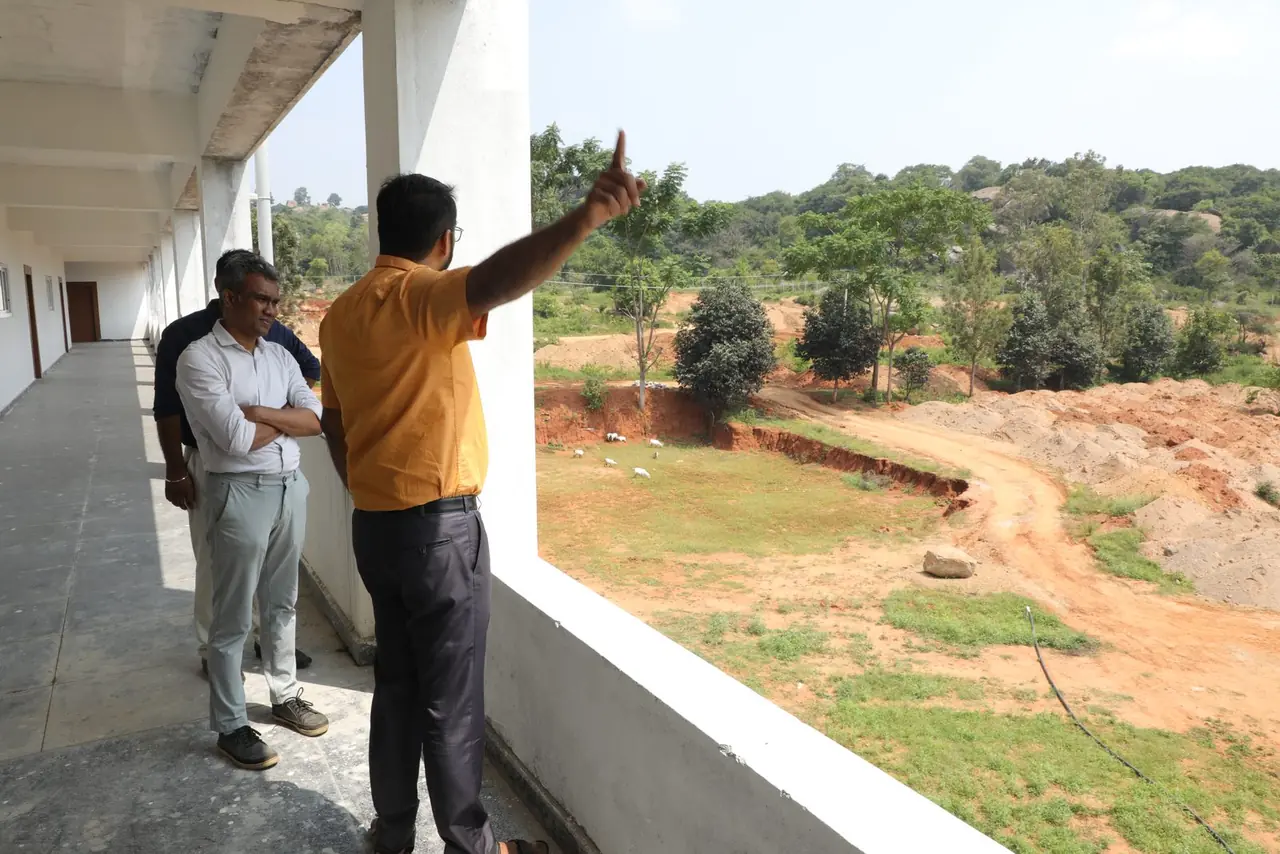 Dr Varun Murthy pointing across the Bachenahatti campus land from the first-floor corridor of the new block