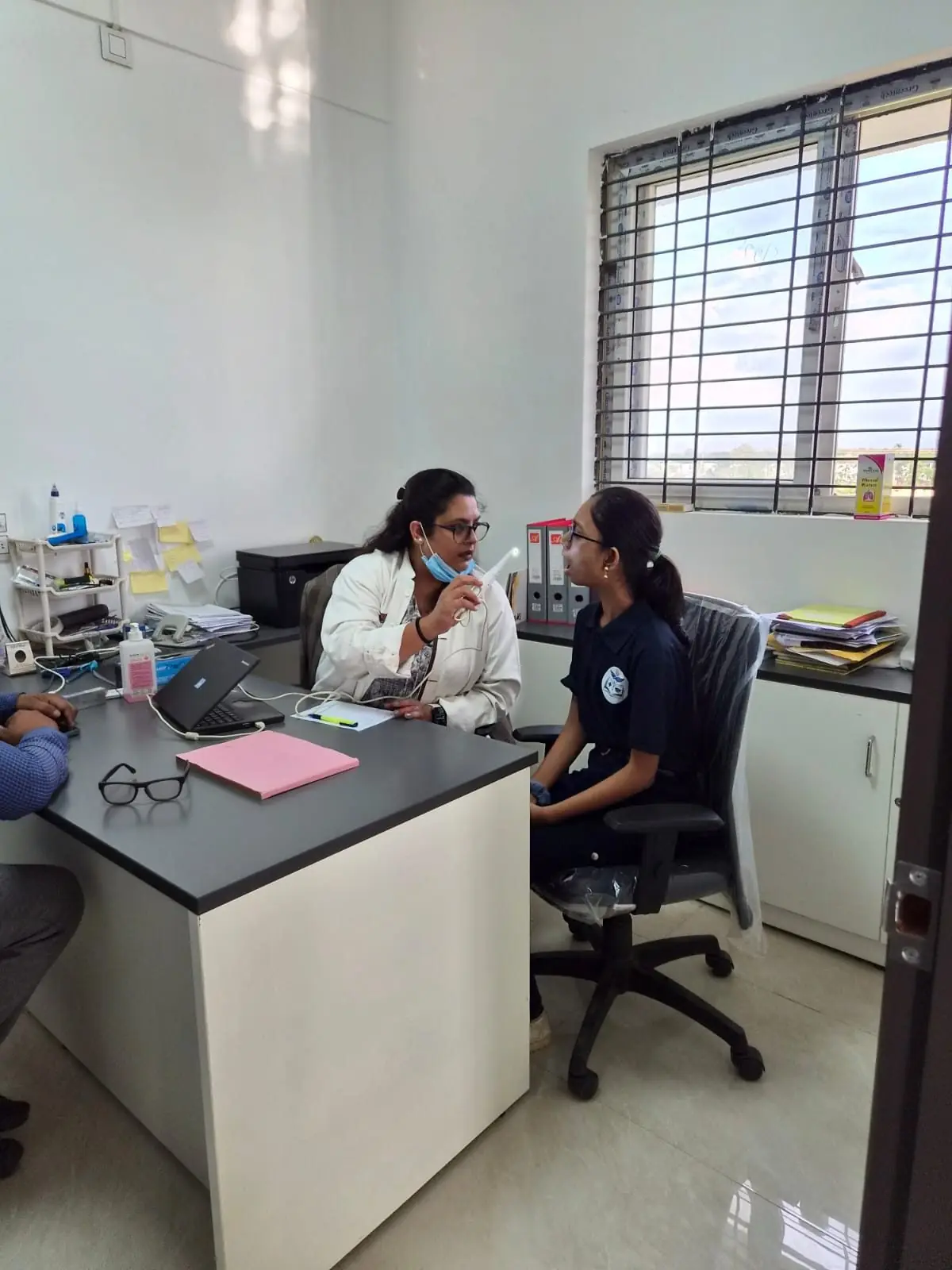A doctor in a white coat talking with a student across a desk