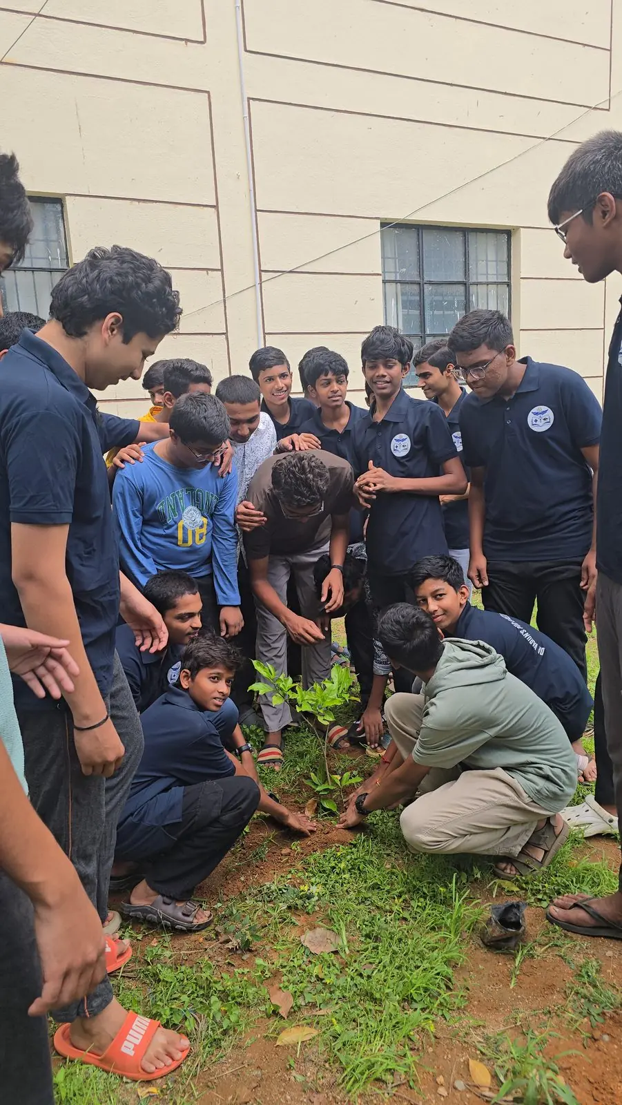 Younger students planting a sapling together on the campus grounds